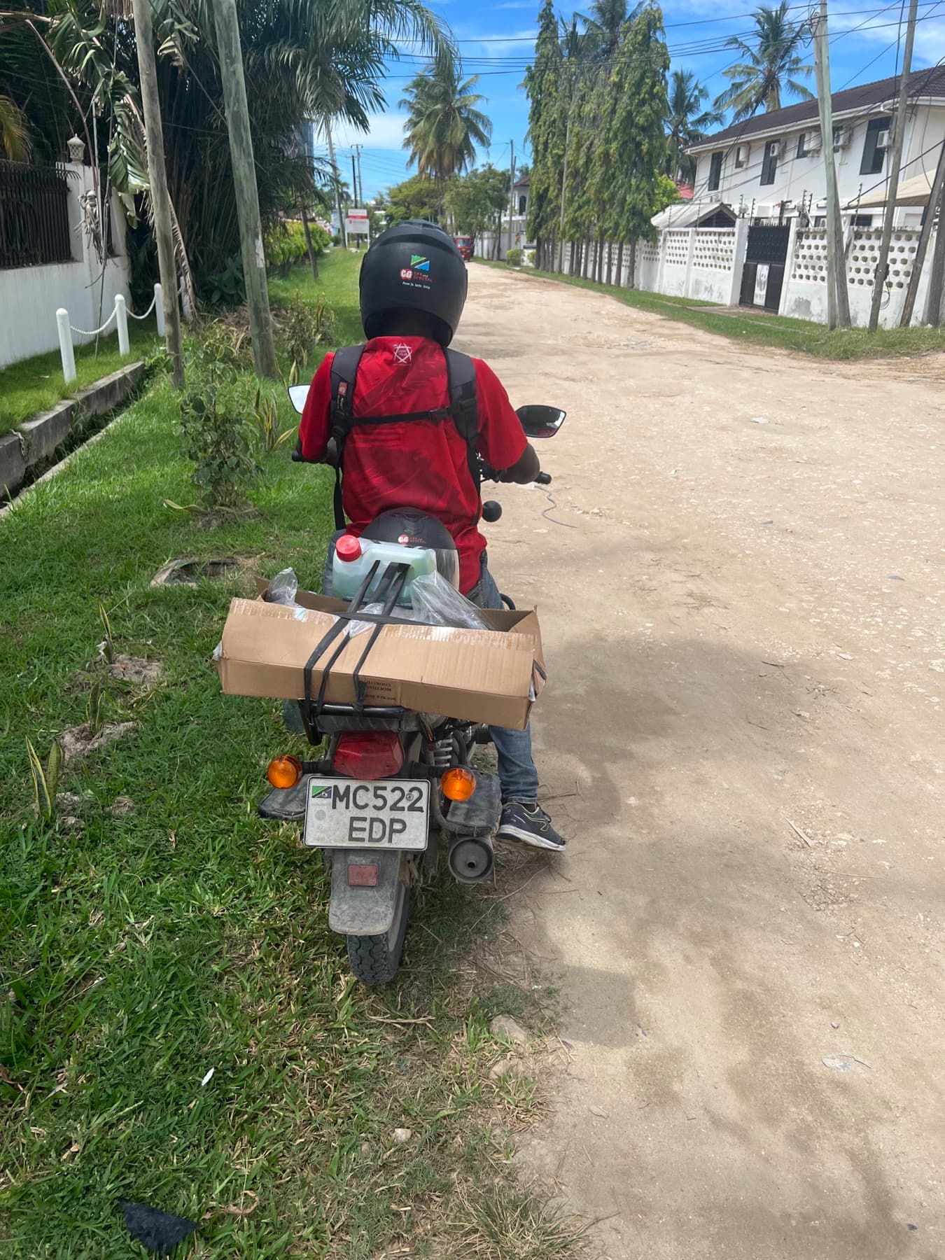A motorcycle rider carrying a boxed container along a residential road